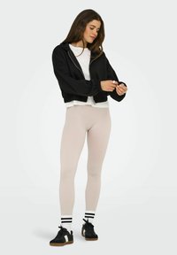 Haut court noir en molleton avec des poignets côtelés, superposé sur une chemise blanche ; associé à des leggings beige côtelés et des baskets noires avec des rayures blanches.