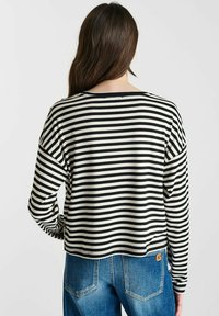 Zwart-witte gestreepte langemouwen top met een losse fit, ronde halslijn en een klein logootje op de zoom, gecombineerd met blauwe denim jeans.