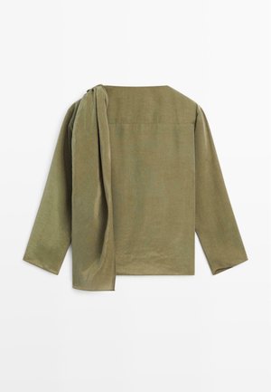 Camicia verde oliva a maniche lunghe con vestibilità ampia, dotata di un'accattivante drappeggio sulla spalla e colletto tondo. Tessuto testurizzato con dettagli minimali.