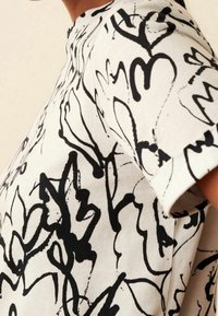 Camiseta de algodón de manga corta con un fondo blanco y dibujos abstractos en negro, de corte relajado y cuello redondo.
