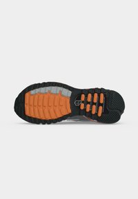 Buitenzool van een sportschoen met een zwart, oranje en grijs profiel, met een getextureerde grip en gesegmenteerde dempingselementen.