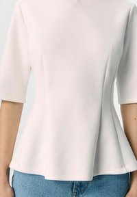 Peplum-Top aus weichem, hellrosa Stoff mit einem hohen Ausschnitt und kurzen Ärmeln. Verfügt über dezente Seitennähte und eine fließende Silhouette.