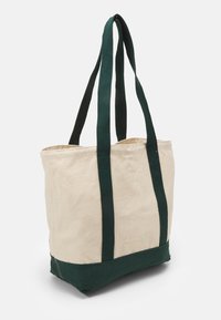 Sac fourre-tout en toile de couleur naturelle avec des anses et un bas vert foncé. Présente un design rectangulaire simple et une construction robuste.