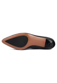 Chaussure en cuir noire à bout pointu vue de dessous montrant une semelle beige avec des inserts noirs antidérapants et un talon bas.
