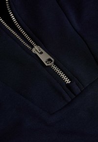 Námořnická látka s kovovým zipem. Hladká textura, obsahující viditelný šev a funkční zip pro snadný přístup.
