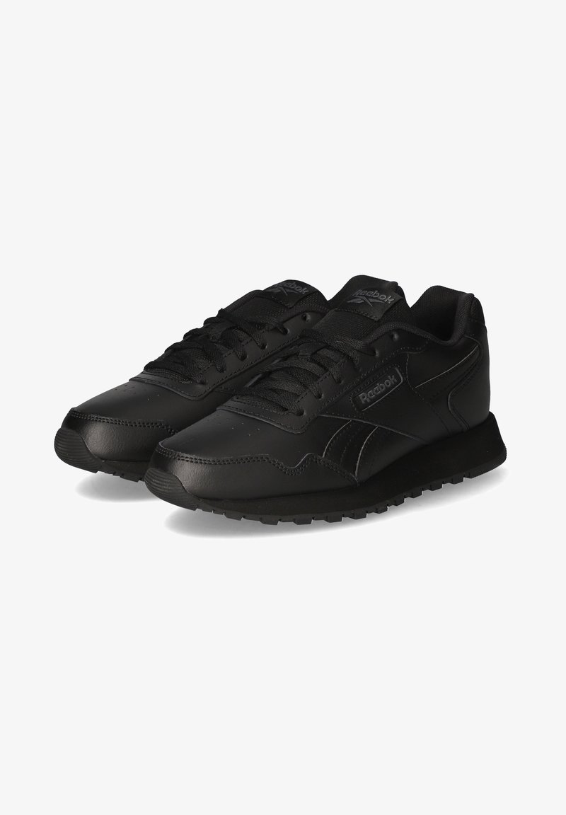Paire de baskets basses Reebok noires avec lacets et semelles en caoutchouc texturé, présentées en angle sur un fond blanc.