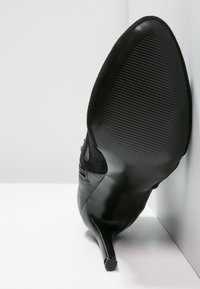 Zapato de tacón alto negro con punta afilada, hecho de cuero liso y ante. Cuenta con una suela texturizada y un tacón de aguja elegante.