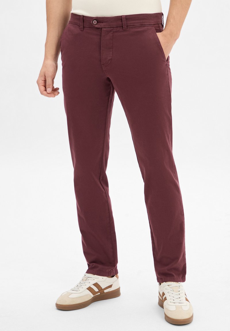 Pantalons en coton bordeaux à coupe slim, avec poches avant et fermeture à bouton. Associés à des baskets crème et marron.
