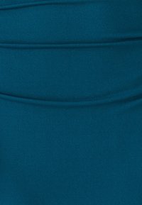 Teal-värinen venyvää kangasta, jossa on sileä pinta, vaakasaumoja ja viivoja, korostaen istuvaa muotoilua. Ei näkyviä kuvioita tai varusteita.