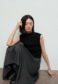 Haut sans manches noir associé à une longue jupe grise fluide. Le tissu semble doux avec une texture mate. Design simple avec des accents minimaux.
