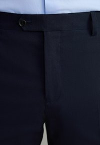 Pantalon bleu marine en tissu texturé, au design épuré, coupe droite et fermeture à un seul bouton à la taille.