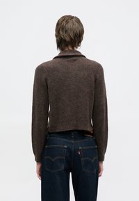 Καφέ πουλόβερ από μαλλί με γιακά σάλι, κοντή γραμμή και μακριά μανίκια, συνδυασμένο με σκούρο μπλε τζιν παντελόνι με αντίθετη ραφή και τσέπες.