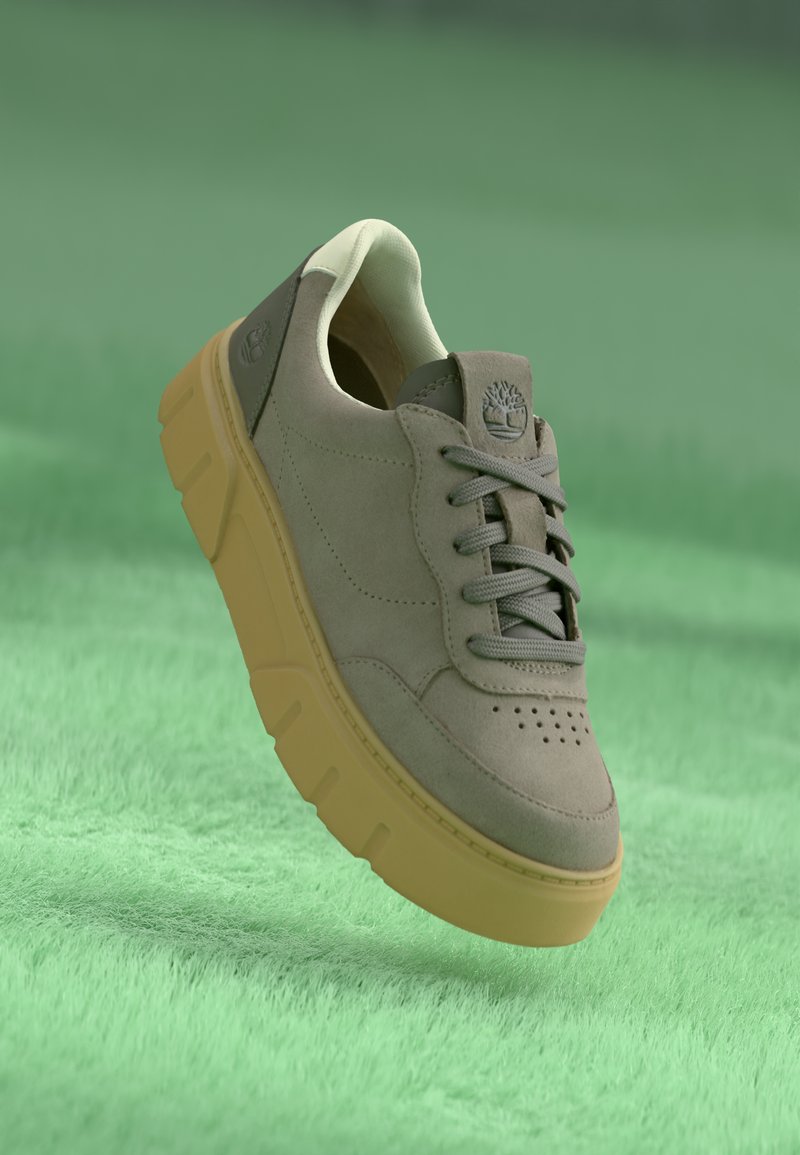 Sneaker din suede gri deschis, cu vârful perforat, șireturi gri și o talpă groasă galbenă. Dispune de un logo pe toc căptușit.