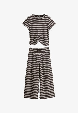 Top negru și alb cu dungi, tricotat cu mâneci scurte și răsucire în față, asortat cu pantaloni evazați tricotati cu dungi similare.