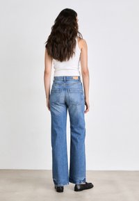 Jeans de tiro alto y pierna ancha de denim, en un lavado claro, con bolsillos traseros y una etiqueta de cuero cosida en la cinturilla.