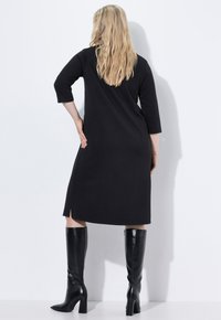 Abito nero al ginocchio con maniche a tre quarti e un motivo testurizzato. Abbinato a stivali neri lucidi e una silhouette elegante.