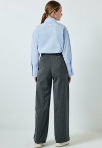 Lichtblauwe shirt met lange mouwen, gecombineerd met hooggetailleerde grijze broek met streep en witte sneakers.
