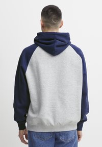 Grå og marineblå hættetrøje med stor hætte, raglanærmer, blød tekstur og ribbede manchetter; bagfra, der viser kontrasterende farveblokke.