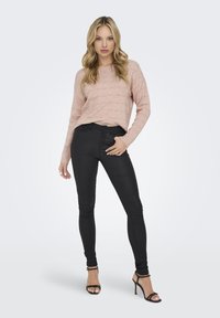 Lichtroze gebreide trui met textuurstreepjes, gecombineerd met zwarte strakke broek en zwarte bandjeshakken. Eenvoudig, modern ontwerp.