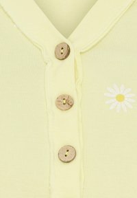 Lys gul ribbet top med tre træknapper og et hvidt pæonedesign på venstre side. Blødt, tekstureret stof med et afslappet design.