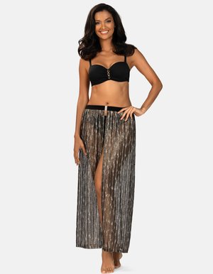 Uśmiechnięta kobieta w czarnym staniku bikini i przezroczystej maxi spódnicy w kolorze czarnym z metalicznymi złotymi akcentami, stojąca boso z ręką na biodrze na białym tle.