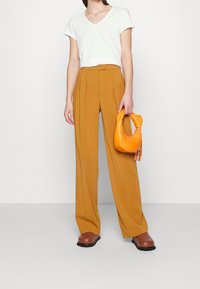Vit t-shirt med V-hals, senapsgula byxor med vida ben, bruna klackskor med blockklack och en orange strukturerad handväska med fransdetaljer.