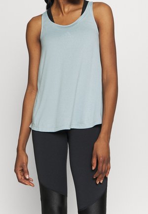 Femme portant un haut sans manches bleu clair par-dessus un soutien-gorge de sport noir et des leggings noirs avec des panneaux brillants sur les cuisses.