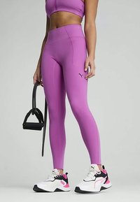 Μωβ ψηλόμεσα κολάν με κομψό σχέδιο, διακοσμημένα με λογότυπα και λεία υφή, σε συνδυασμό με αθλητικά παπούτσια σε λευκό και ροζ χρώμα.