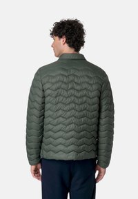 Giacca a vento verde trapuntata con colletto, caratterizzata da una texture a zigzag in rilievo. La giacca ha una forma elegante e compatta ed è leggera.