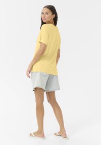 Gul kortærmet t-shirt med en afslappet pasform, parret med lyseblå denimshorts og hvide sandaler, sat mod en ensfarvet baggrund.