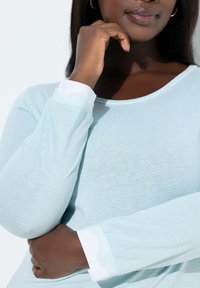 Lyseblå langærmet top med rund halsudskæring og hvide manchetter med blonder. Blødt, tekstureret stof fremhæver komfort.