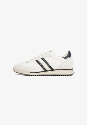 Sapatilha atlética branca com riscas pretas e creme, parte superior de couro liso, sola de borracha e detalhe texturizado no calcanhar. Cadarços e logotipo de lado.