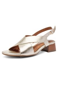 Zlatavě kovový sandál s otevřenou špičkou, překříženými pásky, nastavitelnou přezkou na kotníku a nízkým dřevěným blokovým podpatkem.