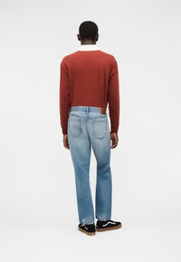 Κόκκινο πουκάμισο με μακριά μανίκια και λευκό γιακά, συνδυασμένο με ανοιχτό μπλε τζιν με δερμάτινο ταμπελάκι. Μαύρα αθλητικά παπούτσια με λευκές λεπτομέρειες.