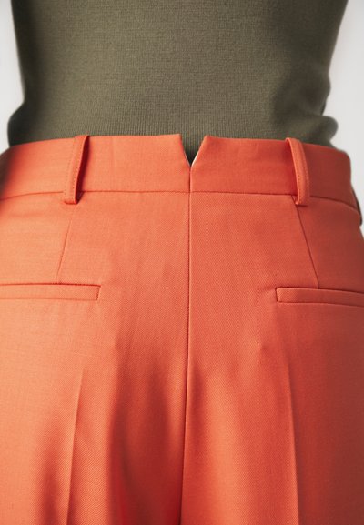 Pantaloni de un portocaliu vibrant, cu un material texturat. Au o talie în formă de V, două buzunare la spate și o croială ajustată.