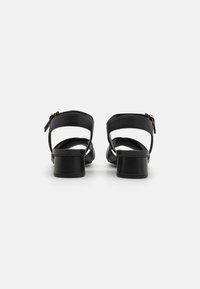 Sandalele cu toc negre au vârf rotunjit, curea reglabilă la gleznă și un toc mai gros. Material din piele moale cu un design minimalist.