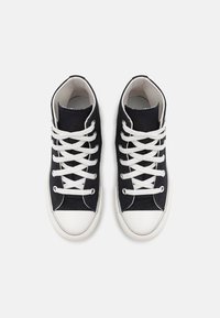 Para czarnych wysokich trampków z kanwy z białymi gumowymi noskami i białymi sznurówkami, widziana z góry na białym tle.