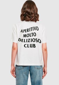 T-shirt en coton blanc avec un grand texte noir au dos indiquant "APERITIVO MOLTO DELIZIOSO CLUB", avec une coupe décontractée et des manches courtes.