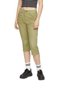 Khaki zkrácené kalhoty s klasickým střihem, hladkým povrchem, předními kapsami a zapínáním na knoflík, v kombinaci s černými botami a pruhovanými ponožkami.