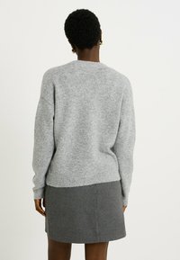 Pull gris en tricot doux avec un col rond, des épaules tombantes et des poignets côtelés, porté sur une jupe grise.