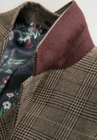Braunes kariertes Blazer mit einem dunkelburgunderfarbenen Kragen. Gefüttert mit einem stoff mit Blumenmuster, das eine Mischung aus Farben und Texturen zeigt.