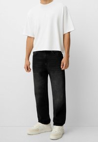 Jeans de mezclilla negros, de corte holgado, con bolsillos frontales. Combinados con una camiseta blanca lisa y zapatillas beige con acentos texturizados.