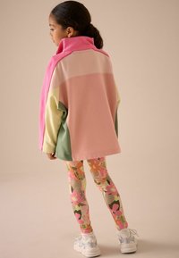 Sweatshirt s velikim blokovima boja u ružičastoj, krem i zelenoj, uparen s tajicama s cvjetnim uzorkom u ružičastoj, narančastoj i bež boji. Bijele tenisice.