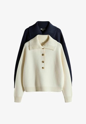 Kremowy sweter z dzianiny z trzema guzikami i szerokim kołnierzem, nałożony warstwowo na czarny sweter z dzianiny z szerokim prążkowanym kołnierzem.