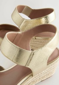 Sandali wedge metallici dorati con una finitura texturizzata, caratterizzati da doppie cinghie larghe e una suola piattaforma in juta intrecciata. Plantare rosa soft.
