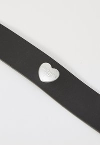 Cinturón de cuero negro con textura suave, que presenta una hebilla metálica en forma de corazón de color plateado grabada con "Carhartt WIP."