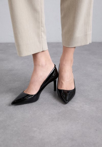 Escarpins en cuir verni noir à talons hauts avec un design à bout pointu et dos ouvert, sur un fond gris clair.