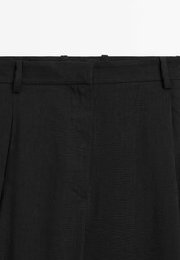 Zwarte broek van een gestructureerde stof, met een platte voorkant, riemlussen en een enkele zijzak. Eenvoudig ontwerp met een op maat gemaakte pasvorm.
