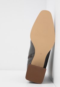 Semelle et talon d'une botte grise à la cheville avec une semelle beige, un talon carré marron texturé, et une fermeture éclair latérale visible, taille 37 marquée sur la semelle.