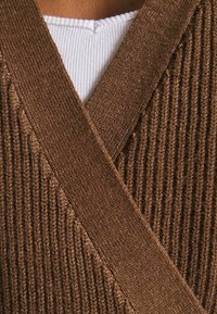 Tissu côtelé marron à finition texturée, avec un design croisé et une couche intérieure blanche contrastante au niveau de l'encolure.